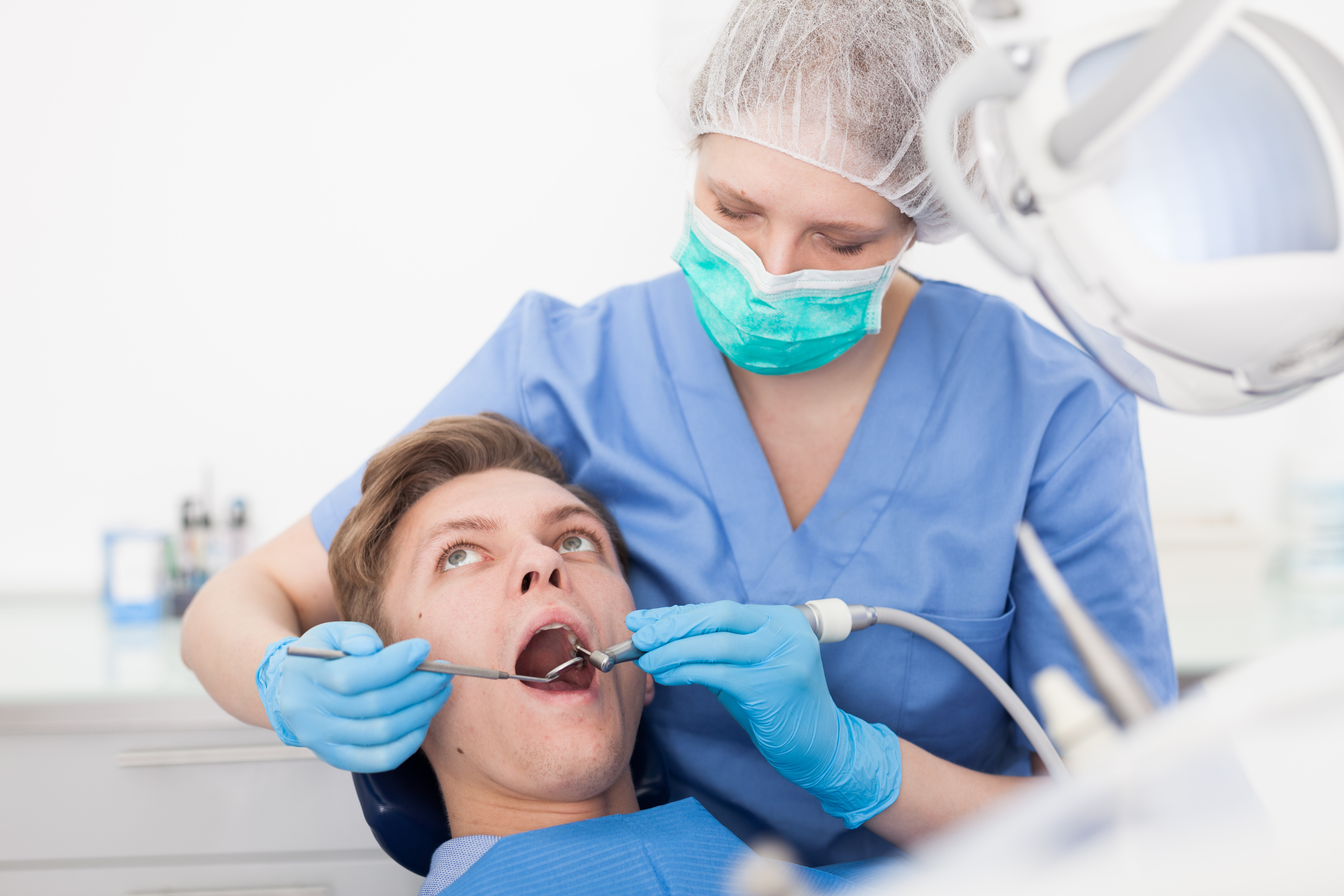 Inlays Zahnarzt Eine Zahnärztin arbeitet mit einem Bohrer und einem Handspiegel an den Zähnen ihres Patienten.