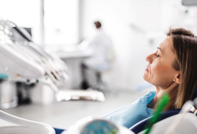 Zahnarztangs Eine Patientin sitzt im Vordergrund auf dem Behandlungsstuhl während der Zahnarzt im Hintergrund auf einem Hocker sitzt.
