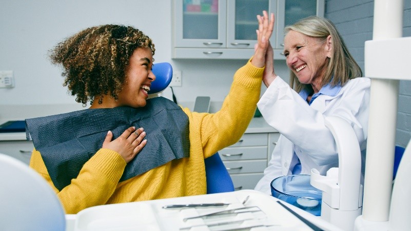 Zahnschmerzen behandelt Eine Patientin und ihre Zahnärztin geben sich ein High Five, während sie lächeln.